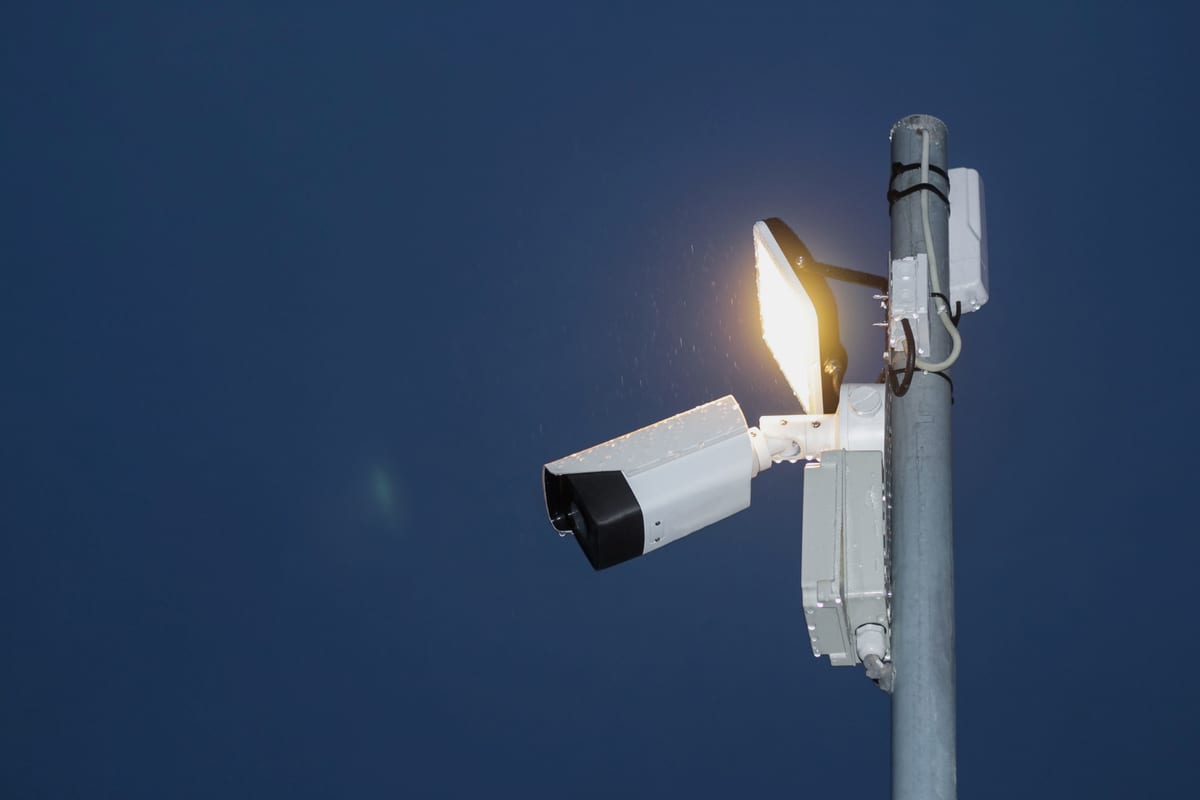 An ANPR camera lit against a dark night sky, reading number plates using infrared light after dark.